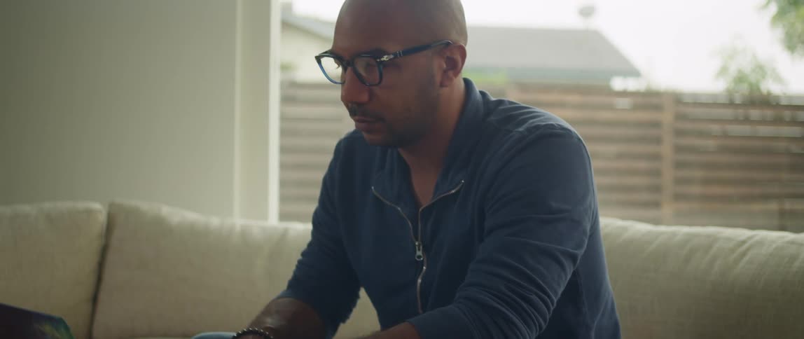A man is sitting on a couch and typing on a laptop