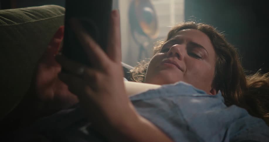 Young happy woman resting on a couch in the living room takes selfies with a smartphone