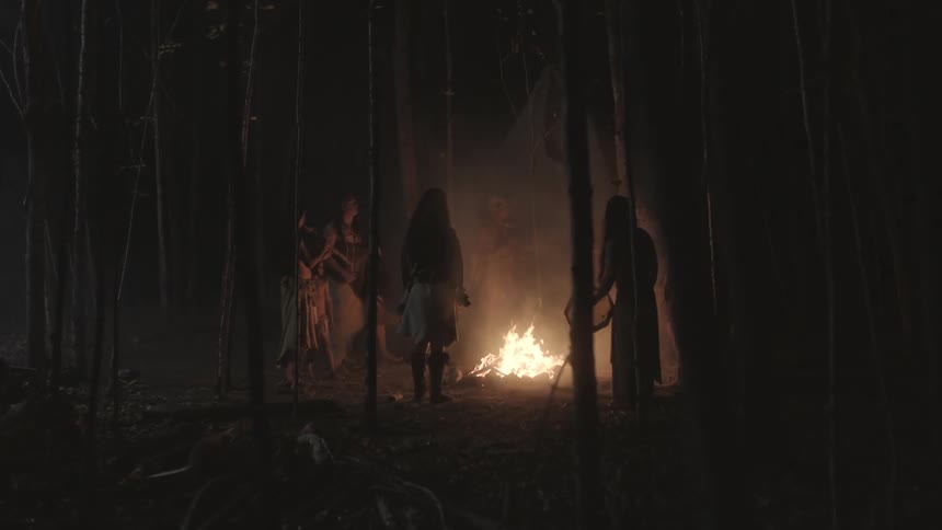A group of native peoples stand around a campfire at night