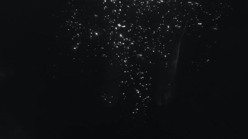 A persons feet move underwater as light reflects on air bubbles as they rise to the surface