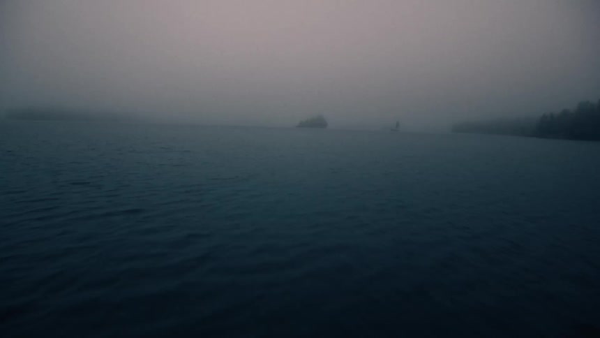 Dense fog covers boat sailing between islet and forested shore