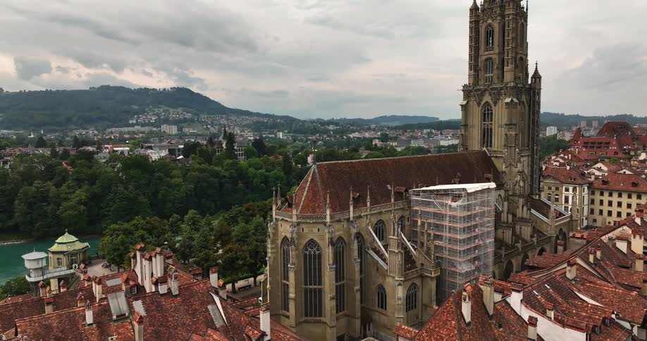 Large medieval building stands surrounded by red roofed buildings in town with forested mountains in the background