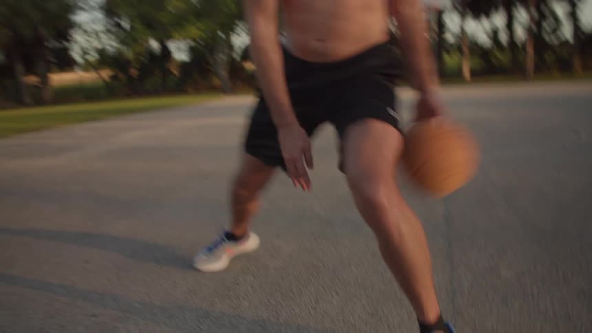 A man is bouncing a basketball on a court in a park then he shoots