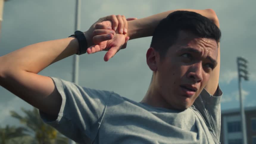 A man stretches one arm behind his back outdoors during the day