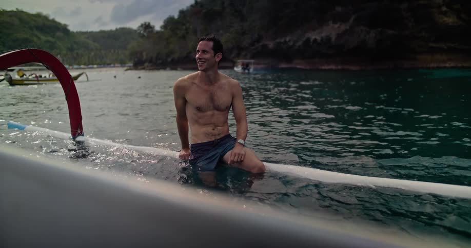 A man sitting in the water on a floating rail smiling near the island