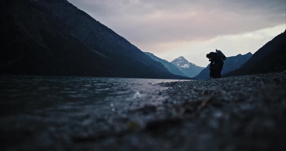 A diver carries equipment along the shore of a lake before preparing for a dive