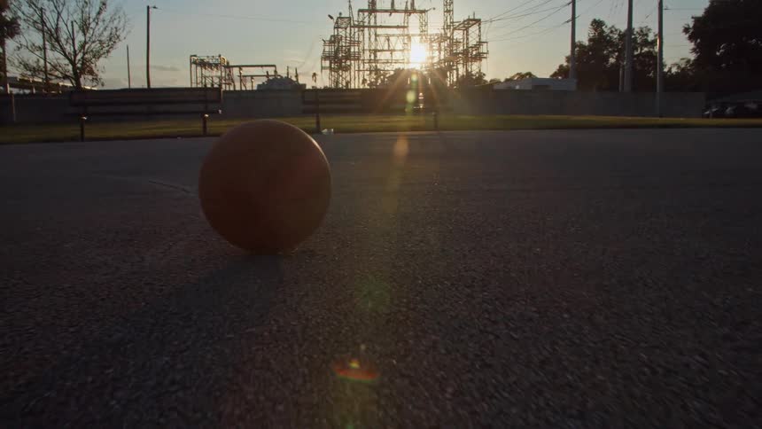 Basketball rolls in basketball court at sunset