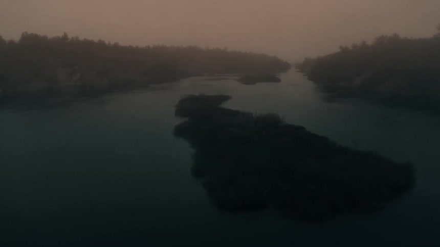 A river splitting a foggy forest under a cloudy evening sky