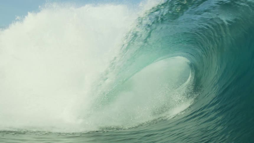 Sunlight shines on a huge wave as it rolls in splashing overhead and then under clear blue water