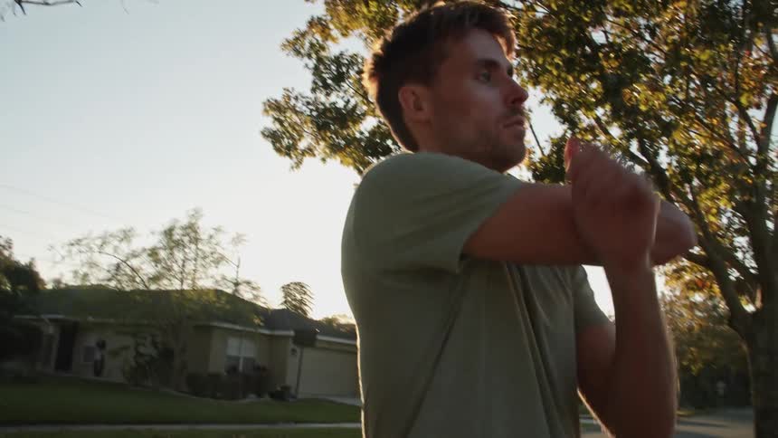 A man stretches his arms while standing outdoors during the day