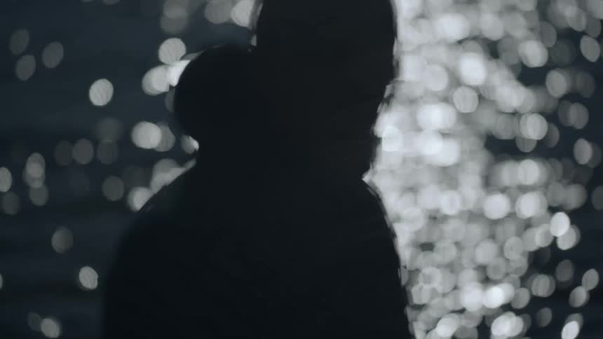 Man wearing coat is silhouetted against the water at sunset