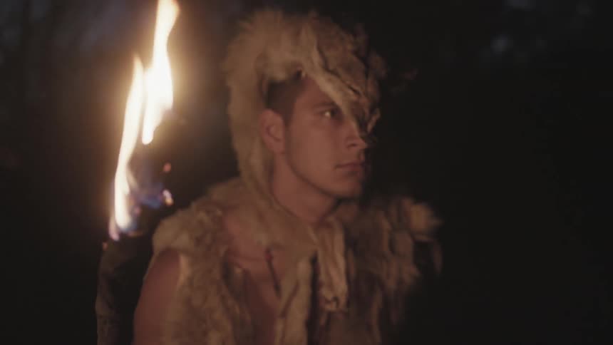 A man carrying a torch standing still in a forest at night