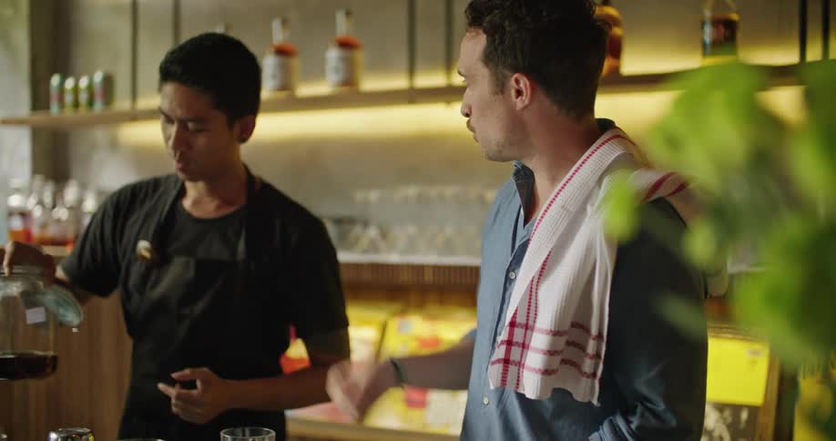 Man standing in bar teaches another man using large partially filled jar