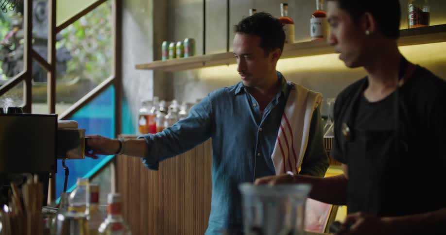 Two men behind a bar turn a dial on a machine as they work