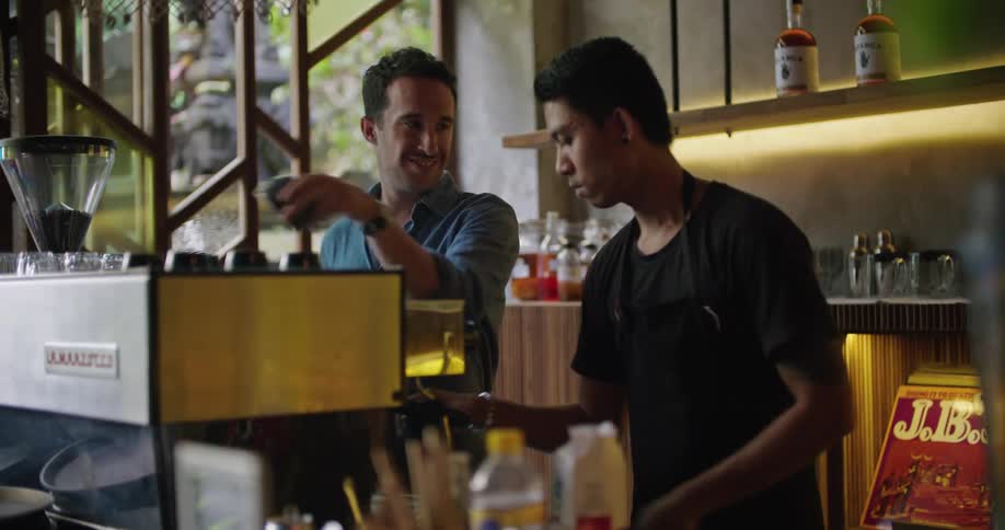 Two men are using an espresso machine in a cafe that has alcohol