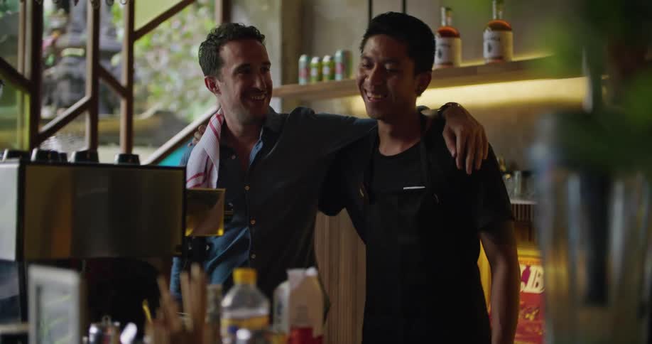 Two bartenders hug while laughing behind the bar counter