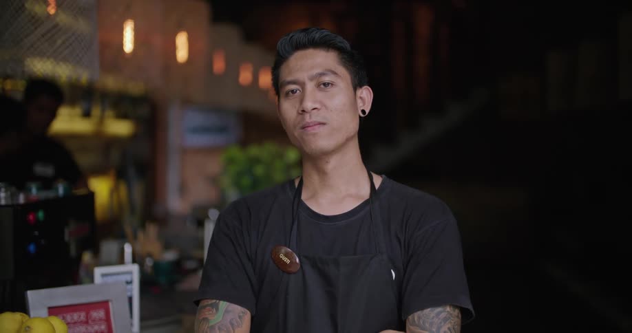 An employee stands in a restaurant with his arms crossed and smiles