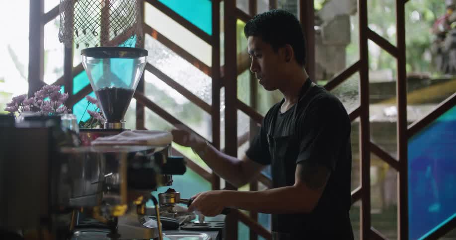 Worker grinds coffee while standing near colorful glass wall