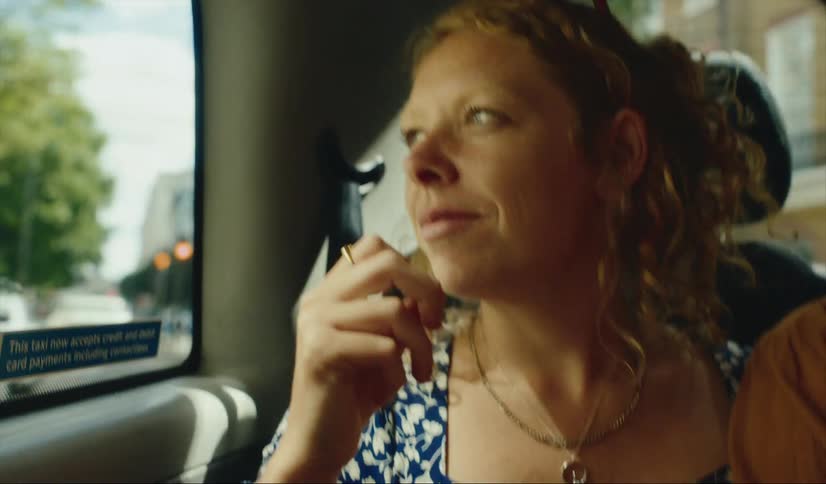 A woman sitting in a London taxi with another person smiles as she looks out the window