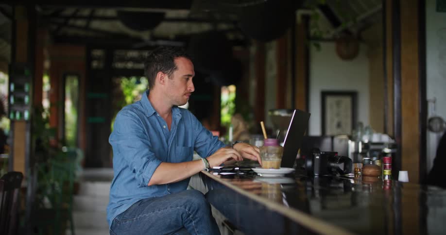 Photographer sits at bar in restaurant using laptop