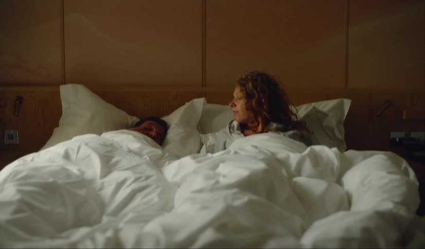 A couple laugh while lying in bed together in a hotel