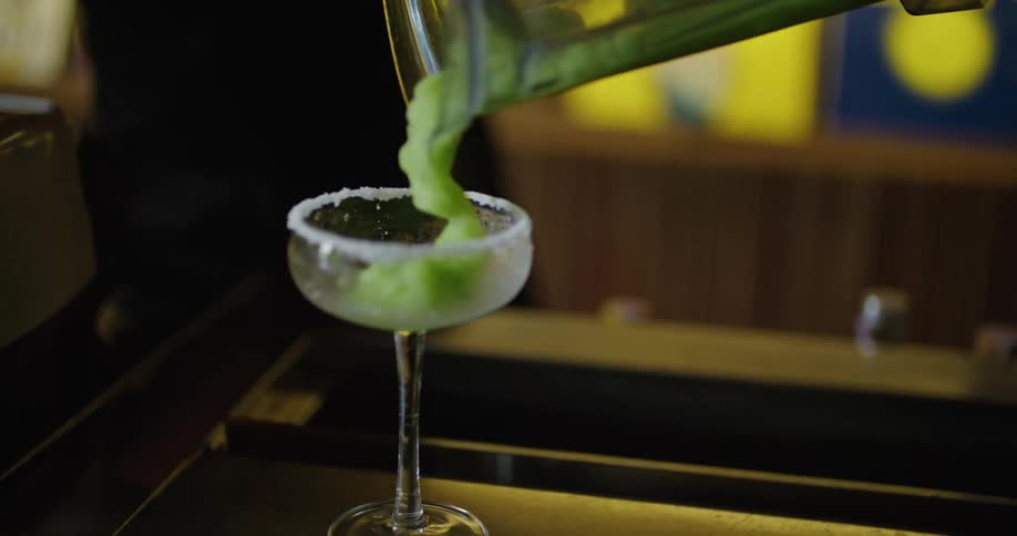 A bartender is pouring a frozen mixed drink out of a blender into a glass