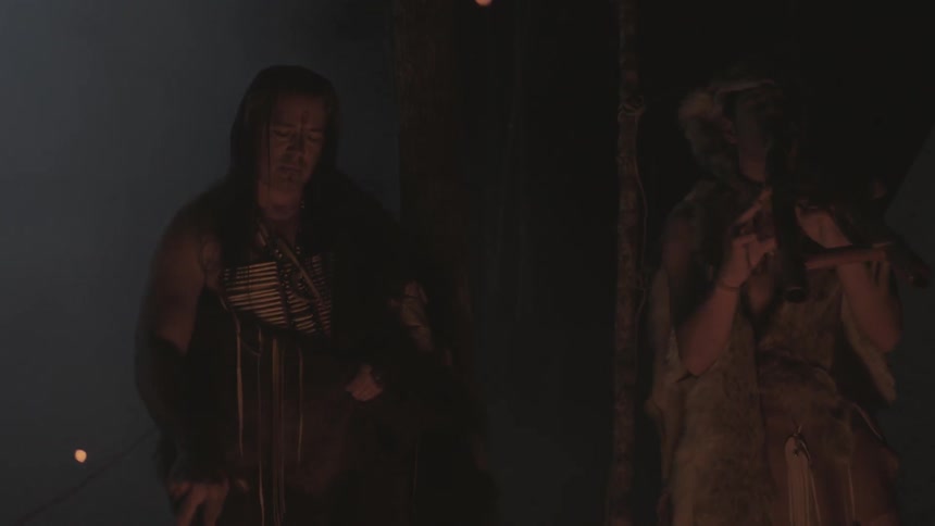 A long haired man pokes a fire