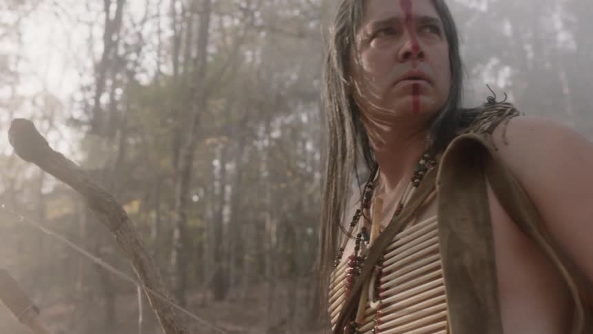 A native american hunter studying his surroundings in a foggy forest