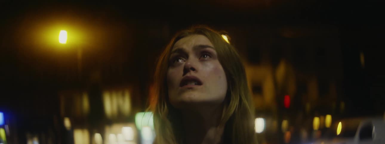 Woman stands downtown at night looking up with teary eyes