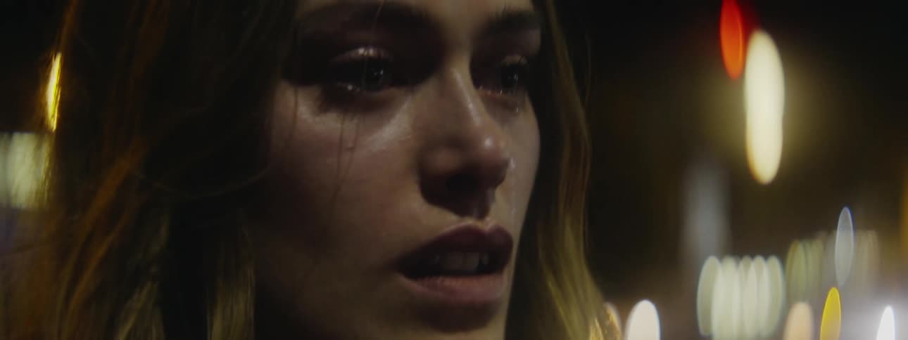 Woman stands staring with teary eyes as traffic passes in the background at night