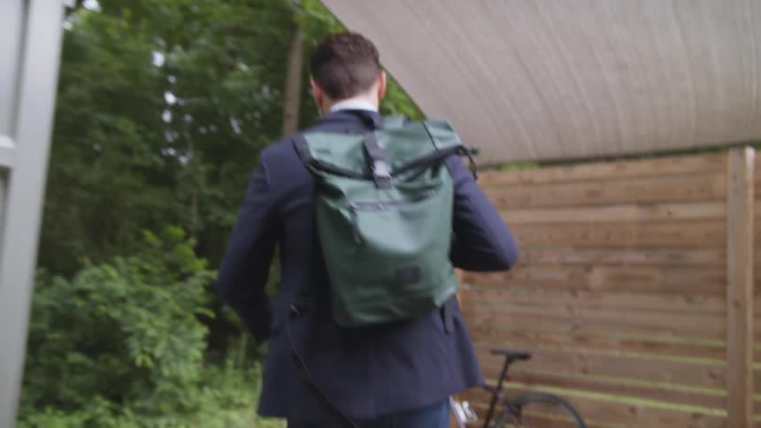 A man walks outside the door as he puts his backpack over his shoulder as he walks to his bicycle
