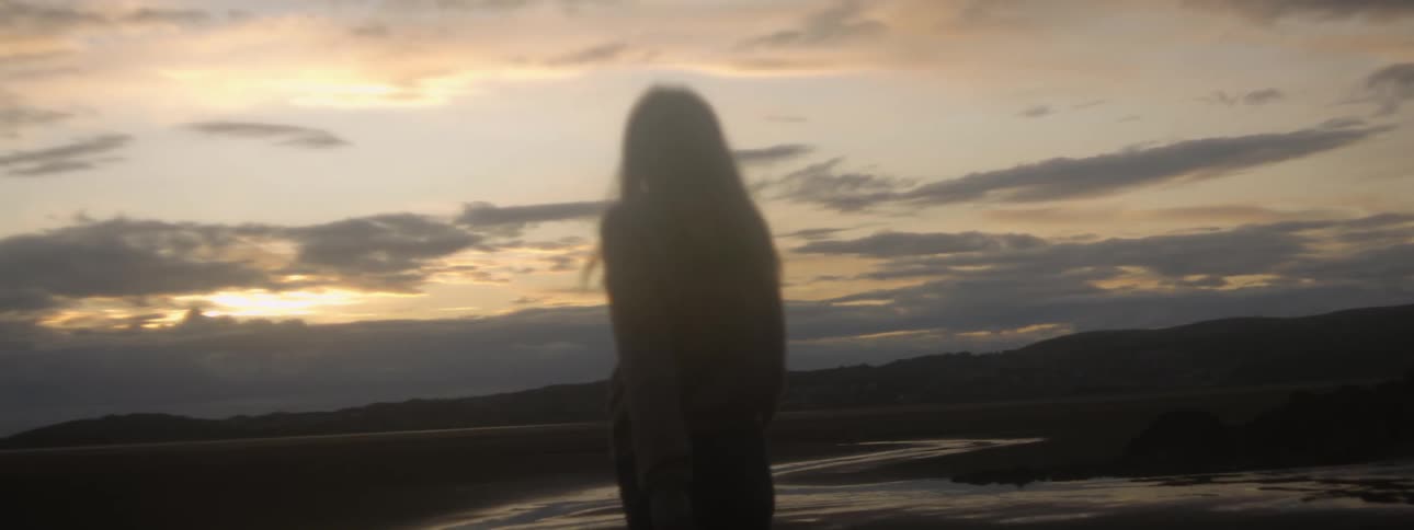 A woman spins around while standing on the beach