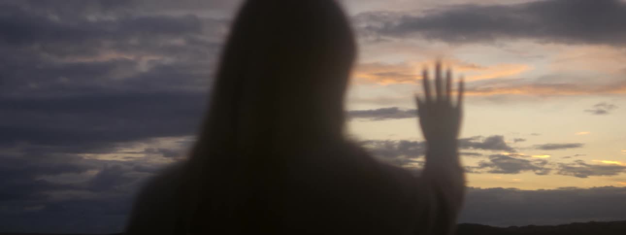 A woman stands outside with her hand in front of her face