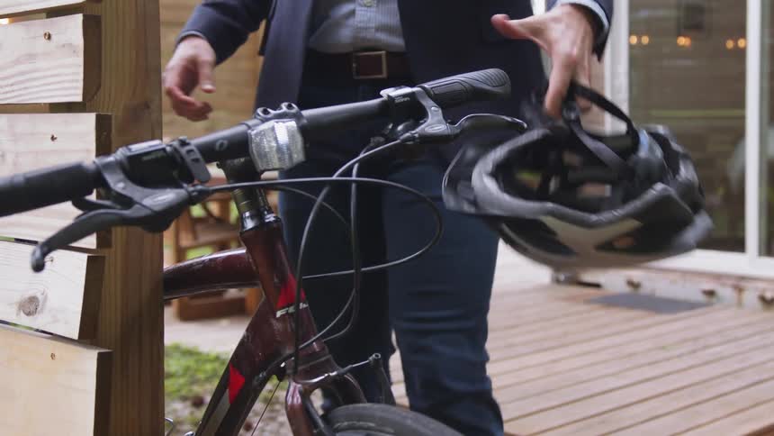 A man walks across a patio as he puts his backpack over his shoulder and walks to his bicycle