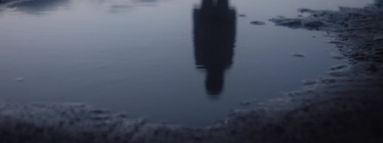 Person is reflected on puddle at dusk