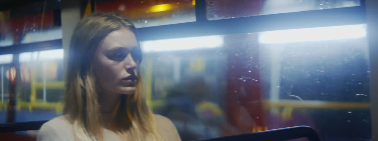 Blonde woman wearing white top sits on bus driving at night