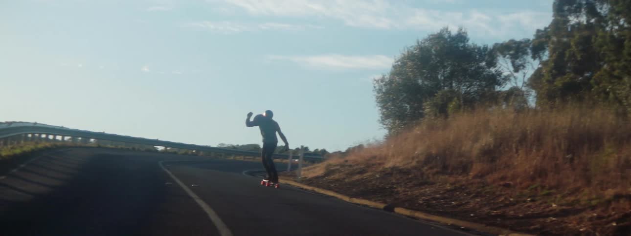 Man rides a skateboard in slow motion downhill on a road at morning