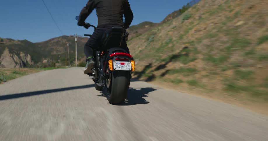 A man wearing dark apparel drives his motorcycle along a remote road