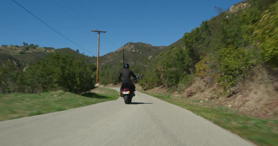 Man wearing black helmet coat and pants rides motorcycle on country road