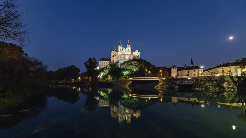 A time lapse of a castle lake houses and trees is shown in fast motion from morning to night