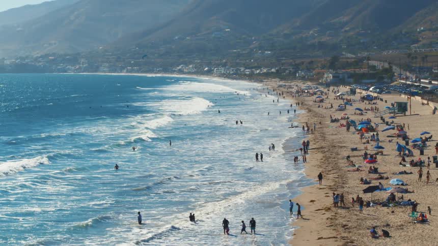 Waves crash as windsurfers and tourists enjoy the beach in Malibu, California