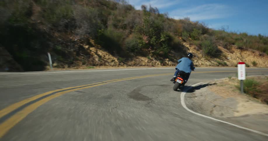 A cyclist rides their motorcycle on a road around a bend on a mountain road