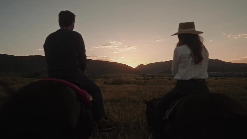 A man and woman chat while sitting on horses in a field