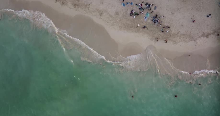 People move along beach as waves crash onto the sand