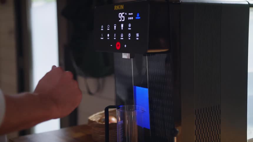 A mans hand is shown pushing buttons on a coffee maker in a kitchen