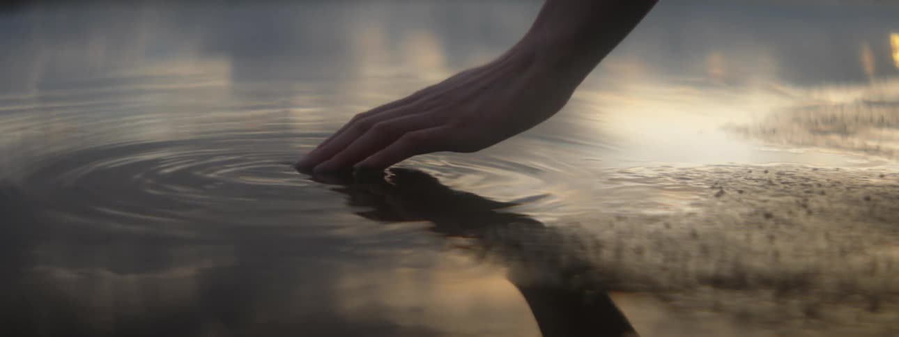 A woman dips her hand in to a lake and runs her fingers through the water