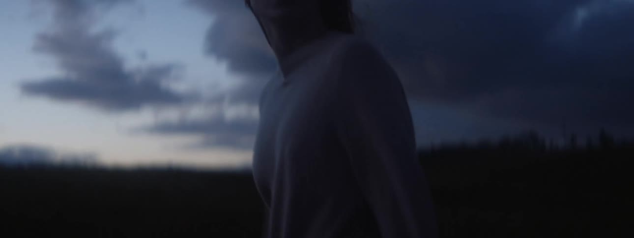 Woman walks quickly under an overcast sky with forest in the background