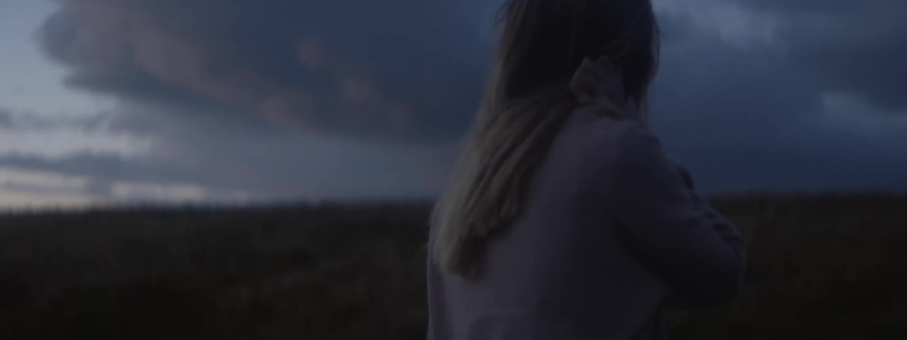 Young blonde woman with long hair walking through a rural field at evening