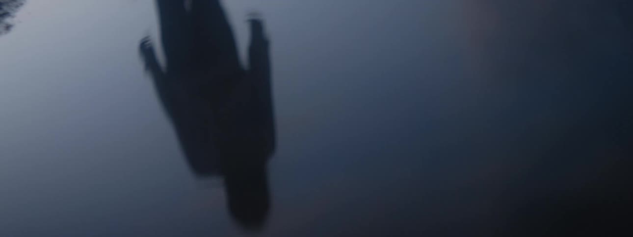 Dark silhouette of a person reflecting on the surface of a puddle at evening