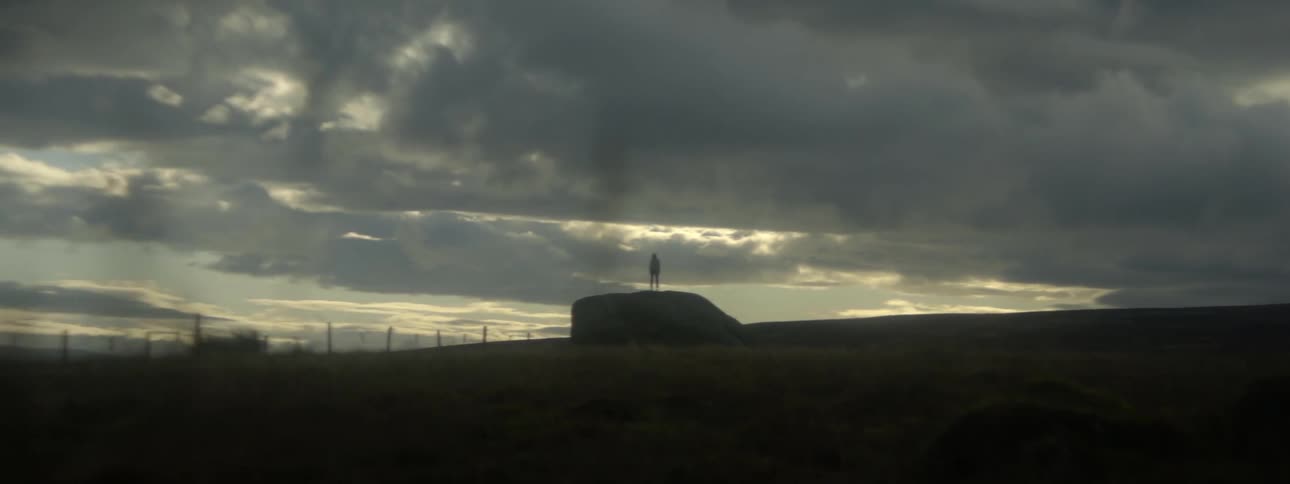 The silhouette of a person can be seen standing far away under a cloudy sky